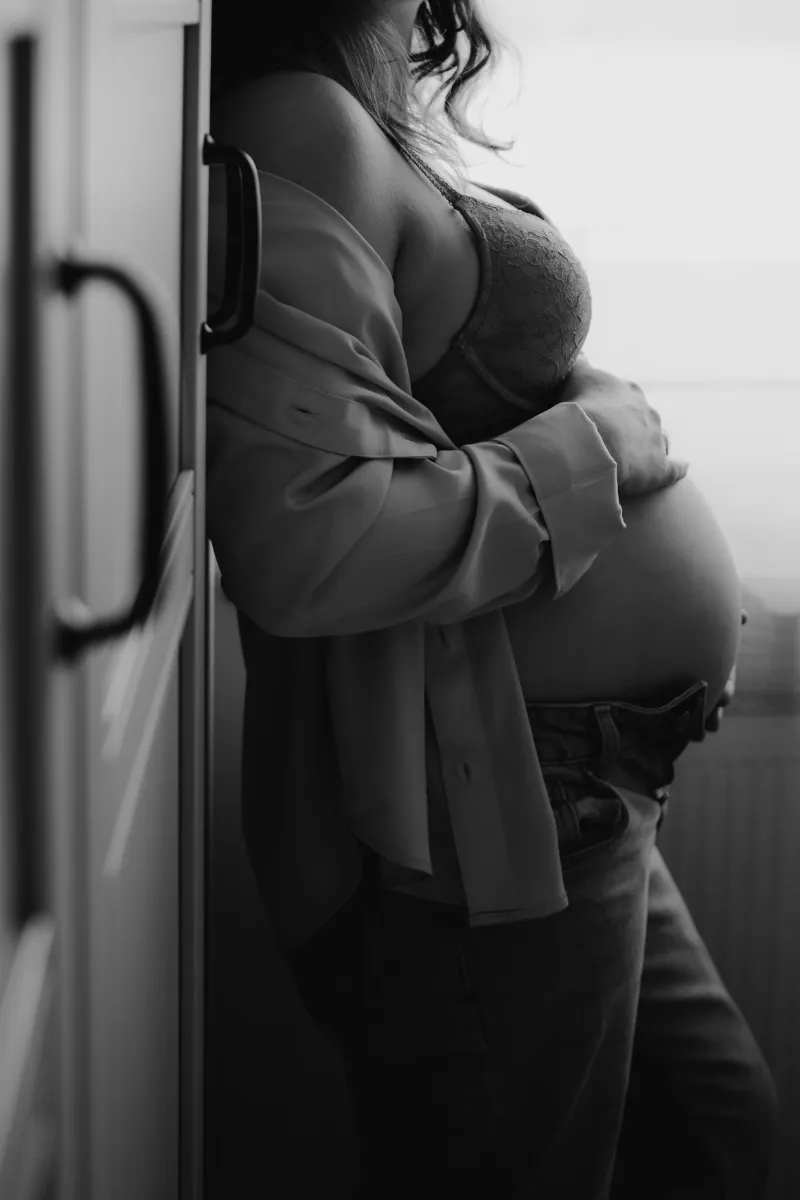 Schwangere Frau vor dem Fenster mit Händen auf dem Bauch