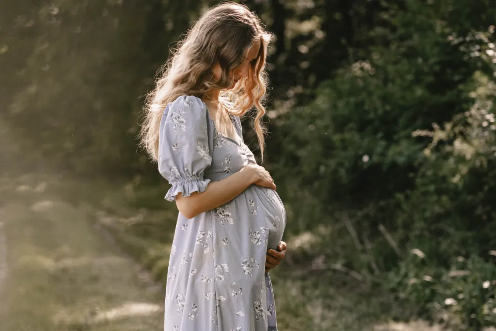 Schwangere Frau im blauen Kleid hält sanft ihren Babybauch