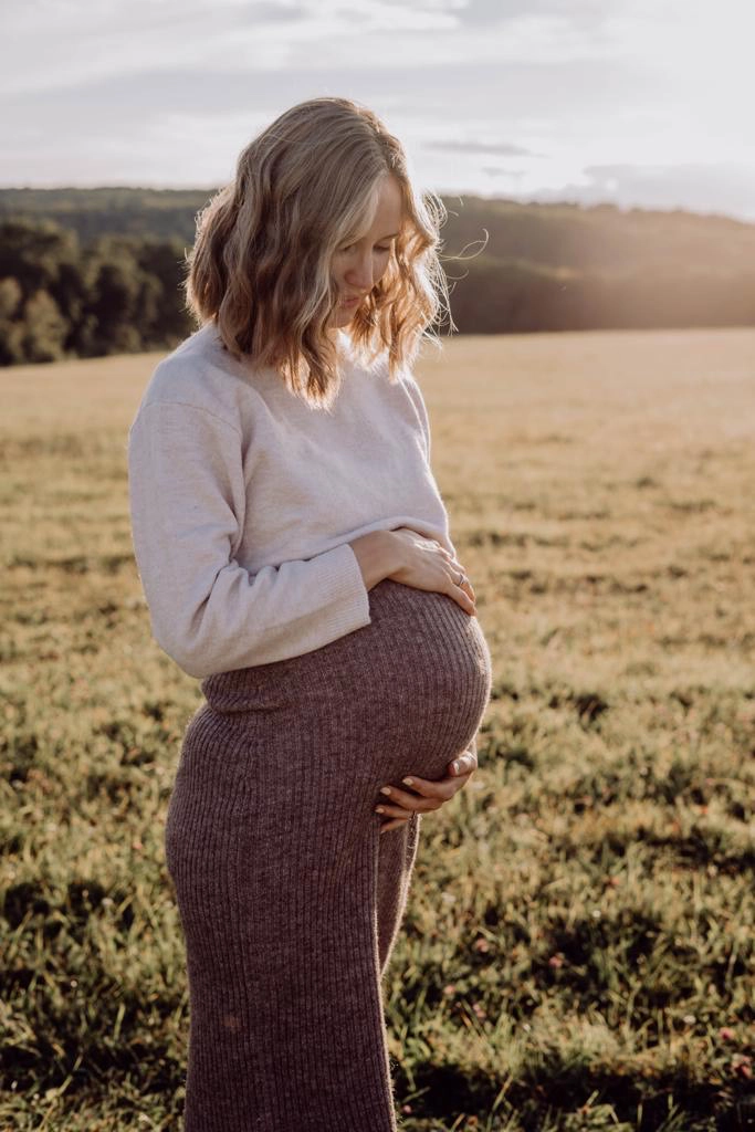 Schwangere Frau vor untergehender Sonne hält sanft Babybauch und lächelt