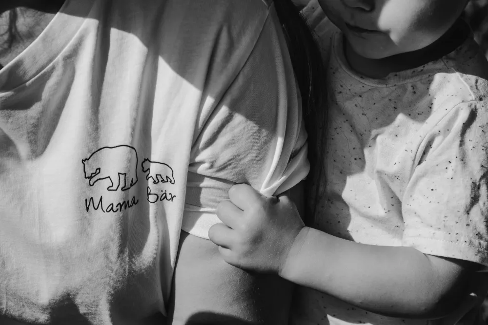 Nahaufnahme kleines Kind krallt sich in Mamas T-Shirt mit Aufschrift Mama Bär