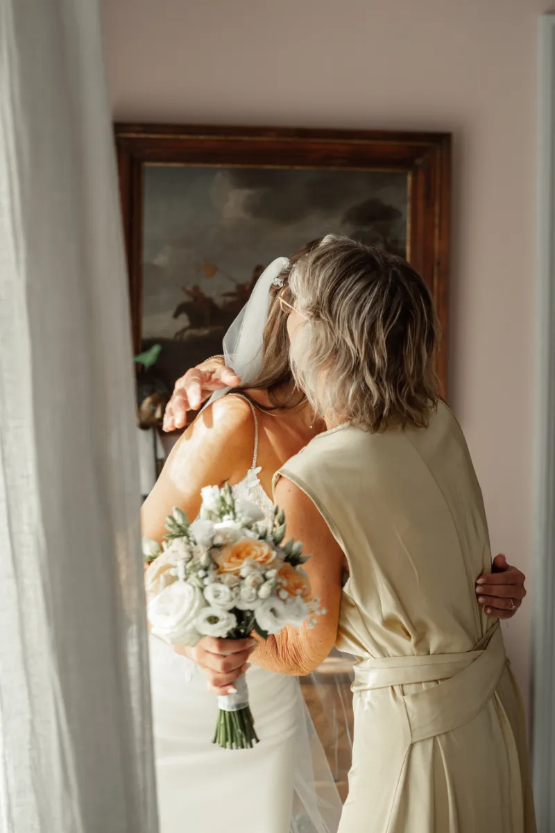 Brautmutter umarmt Braut nachdem sie fertig angezogen ist