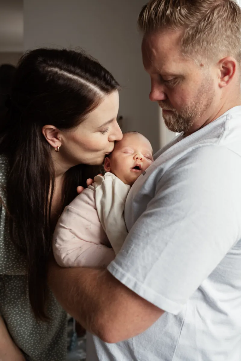 Baby bei Papa auf dem Arm Mama gibt Kuss