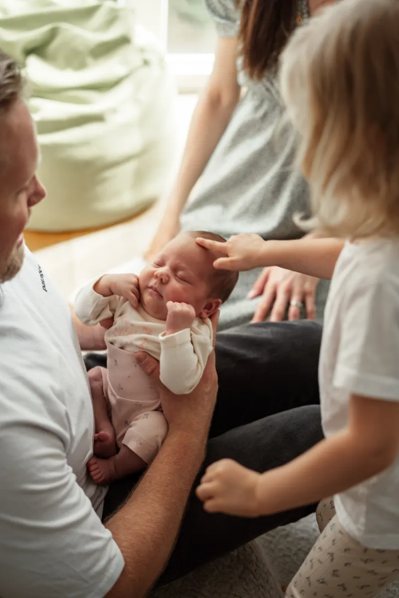 Familie versammelt sich ums Neugeborene bei Papa auf Schoß