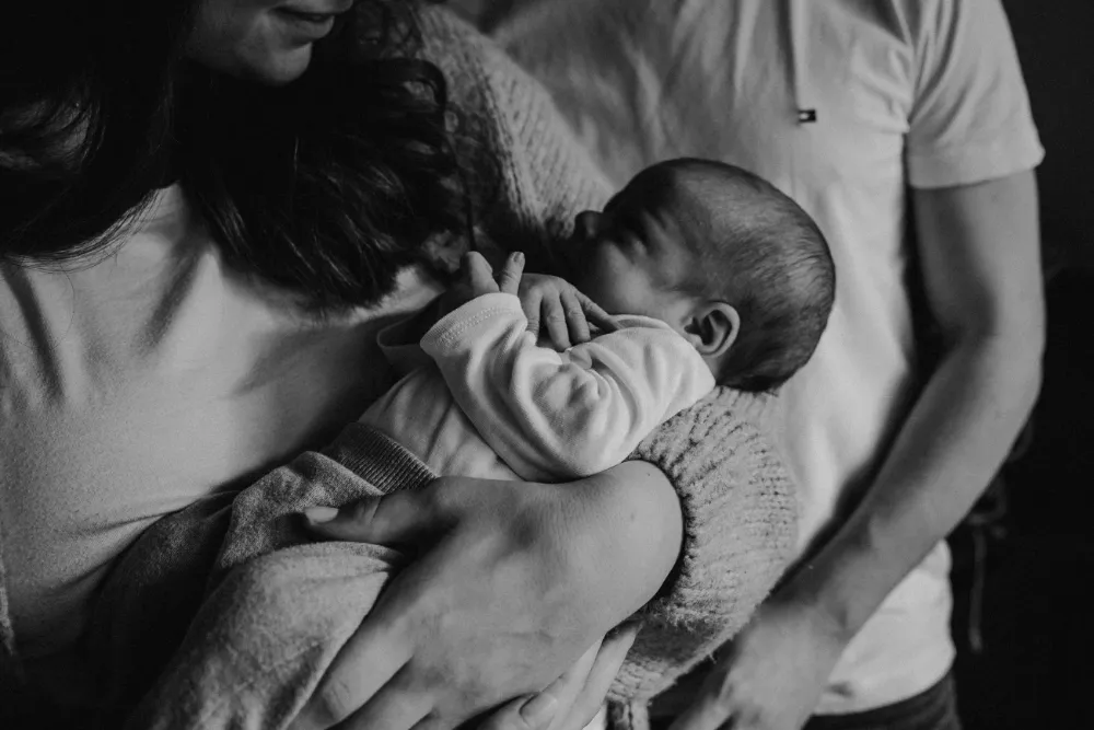 Mutter hält ihr Neugeborenes, Vater im Hintergrund
